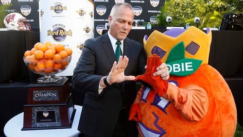 Miami head coach Mark Richt, left, helps Orange Bowl mascot Obie make the Miami "U" symbol as they pose for photos after a news conference, Wednesday, Dec. 6, 2017 in Hollywood, Fla. Wisconsin will play Miami Dec. 30 in the Orange Bowl at Hard Rock Stadium in Miami Gardens, Fla. (AP Photo/Wilfredo Lee)