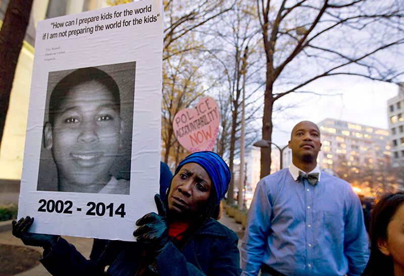 FILE - In this Dec. 1, 2014 file photo, Tomiko Shine holds up a poster of Tamir Rice during a protest in Washington. The 12-year-old black boy was fatally shot by a white Cleveland police officer near a gazebo in a recreational area in November 2014. Officers were responding to a report of a man waving a gun. The boy had a pellet gun tucked in his waistband and was shot right after their cruiser skidded to a stop, just feet away. A grand jury in December 2015 declined to indict patrolman Timothy Loehmann, who fired the fatal shot, and training officer Frank Garmback. The city settled his family's lawsuit for $6 million. The officers still could be disciplined or fired by the department.