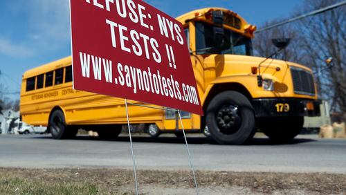 A school bus passes a sign encouraging New York parents to refuse state tests (AP Photo/Mike Groll)