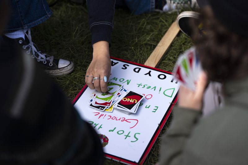 University of Oregon students play Uno on top of a protest sign inside a tent encampment set up on the campus to protest the Israel-Hamas war, Monday, April 29, 2024, in Eugene, Ore. (AP Photo/Jenny Kane)