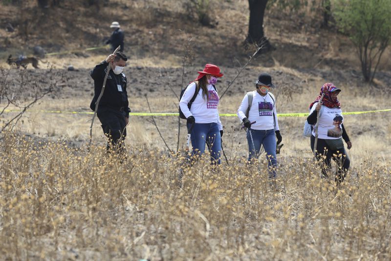 A police officer escorts women carrying digging tools at the site where a clandestine crematorium was found in Tlahuac, on the edge of Mexico City, Wednesday, May 1, 2024. A leader of one of the groups of so-called "searching mothers" from northern Mexico, announced late Tuesday that her team had found bones around clandestine burial pits and ID cards, and prosecutors said they were investigating to determine the nature of the remains. Third from right is Jacqueline Palmeros who has been searching for her disappeared daughter since 2020 in Mexico City, and second from right is María de Jesús Soria whose daughter disappeared in Veracruz in 2016, and whose remains were turned over to her in 2022. (AP Photo/Ginnette Riquelme)