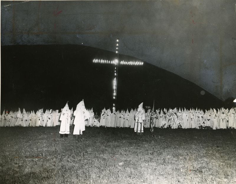 B/W copy of a photo taken in 1948: Hooded Ku Klux Klansmen gather around a huge flaming cross as the Klan held one of its largest initiation ceremonies in its life. In the background looms Stone Mountain. (ACME TELEPHOTO/AJC FILES)