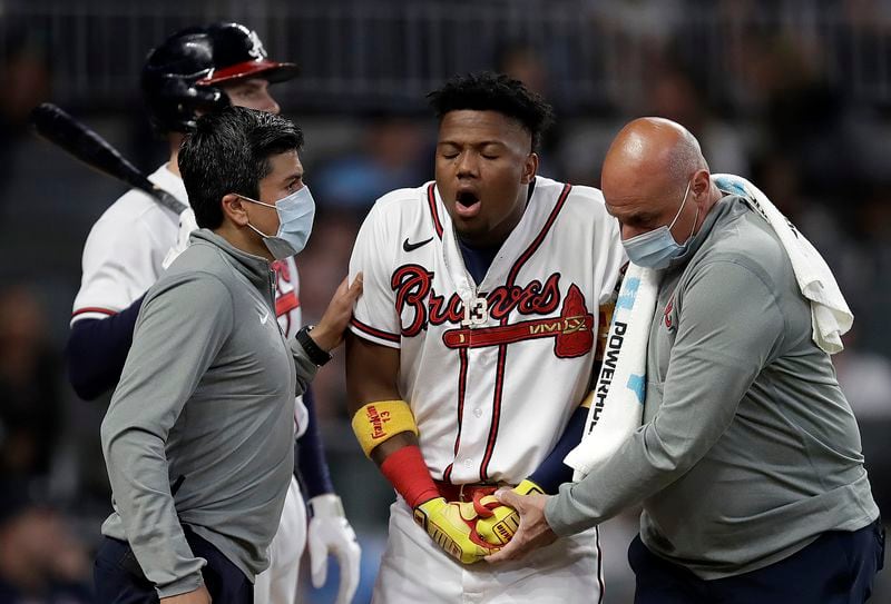 Atlanta Braves' Ronald Acuna Jr., center, is assisted by trainers after being hit by a pitch thrown by Philadelphia Phillies' Sam Coonrod (not shown) in the seventh inning of a baseball game Saturday, May 8, 2021, in Atlanta. (AP Photo/Ben Margot)
