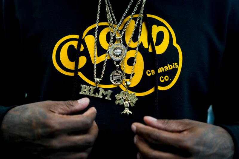 Cloud 9 Cannabis CEO and co-owner Sam Ward Jr. wears chains among over a custom hoodie, Saturday, April 13, 2024, in Arlington, Wash. The shop is one of the first dispensaries to open under the Washington Liquor and Cannabis Board's social equity program, established in efforts to remedy some of the disproportionate effects marijuana prohibition had on communities of color. (AP Photo/Lindsey Wasson)