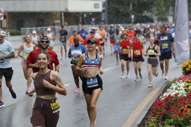 Runners pass along Peachtree Road in Buckhead with light rain at the beginning of the course during the 54th running of The Atlanta Journal-Constitution Peachtree Road Race in Atlanta on Tuesday, July 4, 2023.  The race would later end early because of the weather turning severe.  (Miguel Martinez / Miguel.Martinezjimenez@ajc.com)