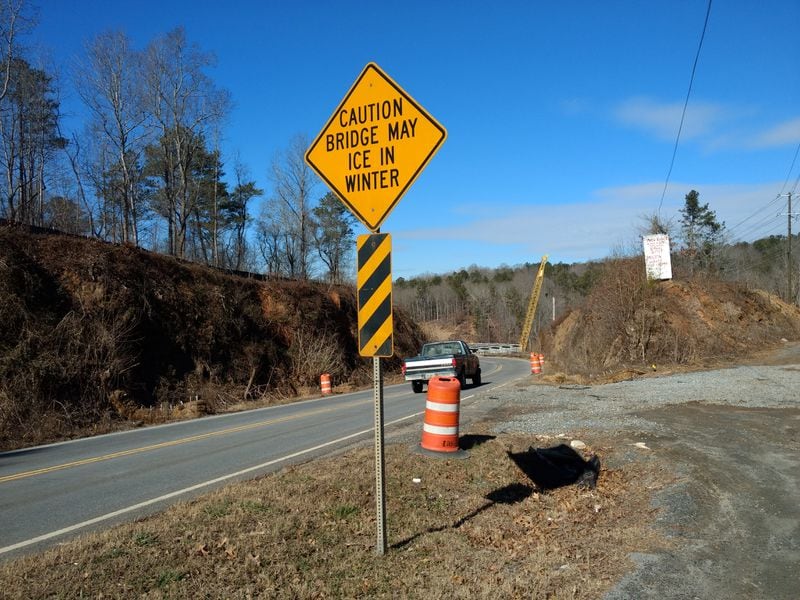 This bluff on the right side of the road has been leveled. This photo was taken on the Milton side. The bridge construction can be seen beyond the pickup truck. A construction crane is visible just above the bridge.