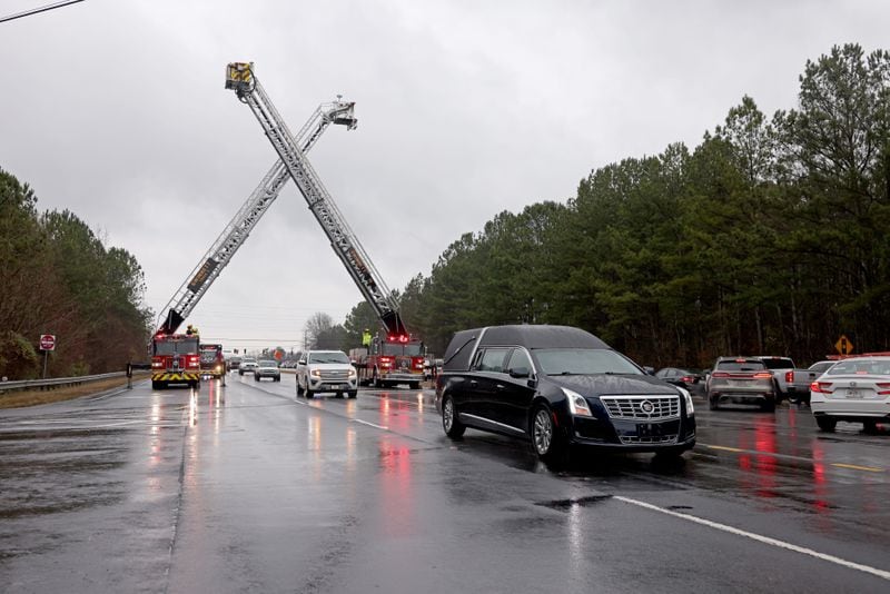 The hearse carrying the remains of Gwinnett County correctional officer Scott Riner goes underneath Gwinnett County fire trucks during the procession for Riner on Buford Drive, Tuesday, December 20, 2022, in Lawrenceville, Ga.. (Jason Getz / Jason.Getz@ajc.com)