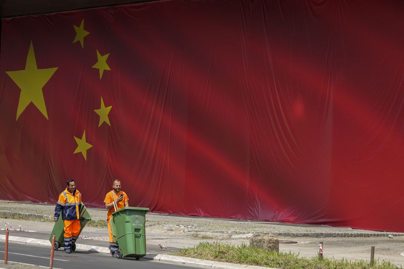 Cleaners walk in front of a Chinese national flag placed on the building in Belgrade, Serbia, Tuesday, May 7, 2024. Chinese leader Xi Jinping's visit to European ally Serbia on Tuesday falls on a symbolic date: the 25th anniversary of the bombing of the Chinese Embassy in Belgrade during NATO's air war over Kosovo. (AP Photo/Darko Vojinovic)