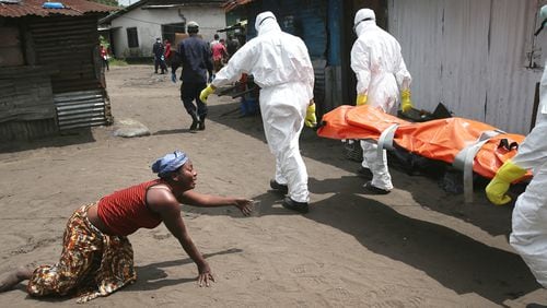 A woman crawls towards the body of her sister as Ebola burial team members take her sister Mekie Nagbe, 28, for cremation on Oct. 10, 2014 in Monrovia, Liberia.