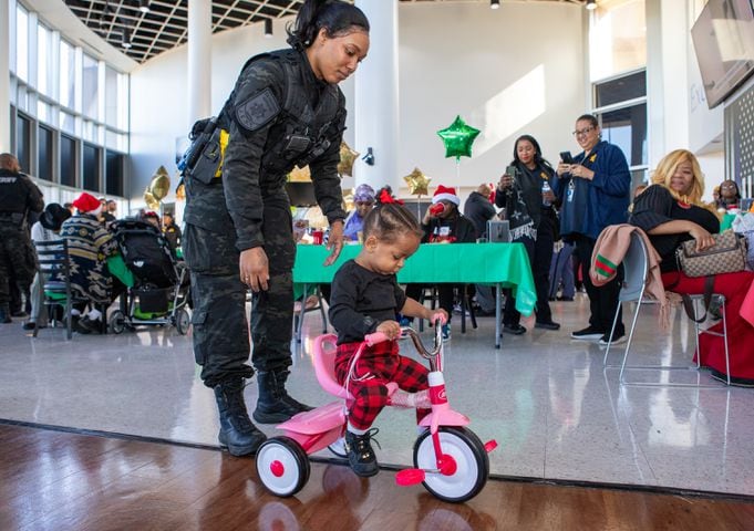 DeKalb County Sheriff’s Office holds the 16th annual Adopt-A-Family celebration on Tuesday, Dec 16, 2023 where Officer Davis, left, helps 3-year old Olivia Banks with her new bike. Law enforcement officers donate their own money and buy gifts for about a dozen local children.  (Jenni Girtman for The Atlanta Journal-Constitution)