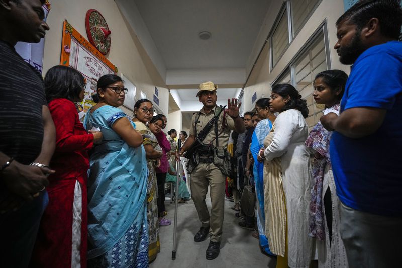 A security person stops a person who tried to break the queue as people wait to cast their votes in a polling station during the third phase of general election in Guwahati, India, Tuesday, May 7, 2024. (AP Photo/Anupam Nath)