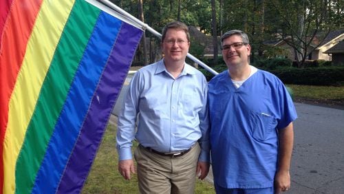 Gary Caudill (left) and his partner, Matt Lombardi, stand before the rainbow flag that’s been on display at their Peachtree Corners home since June to celebrate Gay Pride Month. The couple was about to take the flag down when an anonymous resident complained the emblem is offensive. GRACIE BONDS STAPLES / GSTAPLES@AJC.COM