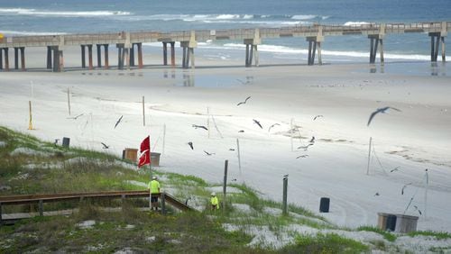 In this March 23, 2020 photo, workers take advantage of the lack of beachgoers to do some repairs to the dune walkover bridges along Jacksonville Beach in Jacksonville, Fla. Mayor Lenny Curry says Duval County beaches are reopening Friday, April 17, 2020, with restricted hours, and they can be used only for walking, biking, hiking, fishing, running, swimming and surfing. (Bob Self/The Florida Times-Union via AP)