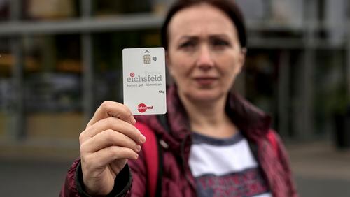 Erdina Laca, a 45-year-old asylum seeker, shows her special payment card in front of a grocery store, in Eichsfeld, Germany, Wednesday, April 24, 2024. Across Germany, cities and counties are introducing new payment cards for asylum-seekers. The new rule, which was passed by parliament last month, calls for the migrants to receive their benefits on a card that can be used for payments in local shops and services. (AP Photo/Ebrahim Noroozi)