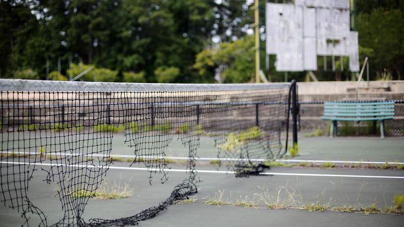 In this July 19, 2016, photo, the derelict netting and scoreboard in the background on a tennis court stand at the Stone Mountain Tennis Center, home of the 1996 Summer Olympic Games tennis events, in Stone Mountain, Ga. The permanent tennis facility built in a corner of Stone Mountain Park quickly became a money loser and now sits idle, weeds growing through the outer courts and the scoreboard in disrepair. (AP Photo/David Goldman)