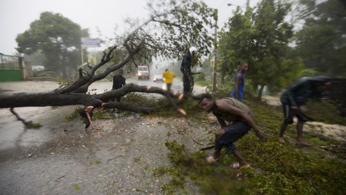 People work to remove an uprooted tree from a road in Leogane, Haiti. Tuesday, Oct. 4, 2016. Matthew slammed into Haiti's southwestern tip with howling, 145 mph winds Tuesday, tearing off roofs in the poor and largely rural area, uprooting trees and leaving rivers bloated and choked with debris. ( AP Photo/Dieu Nalio Chery)
