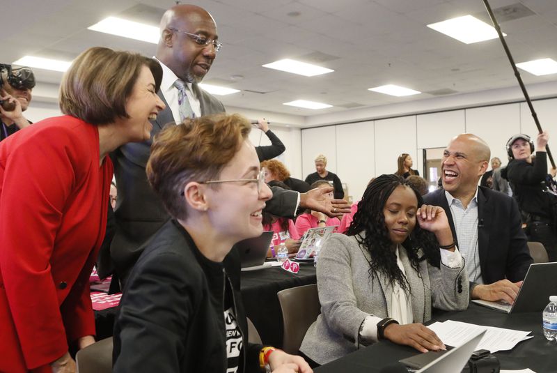 Democrat Raphael Warnock, standing, shares a moment with Democratic U.S. Sens. Amy Klobuchar and Cory Booker, far right, at a phone bank while the two senators were in Atlanta to participate in debate between Democratic presidential candidates. Warnock hopes to join them in the U.S. Senate.