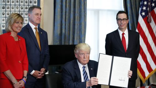President Donald Trump, accompanied by, from left, Rep. Claudia Tenney, R-N.Y., Sen. David Perdue, R-Ga., and Treasury Secretary Steve Mnuchin, holds up a signed Executive Order, Friday, April 21, 2017, at the Treasury Department in Washington. (AP Photo/Alex Brandon)