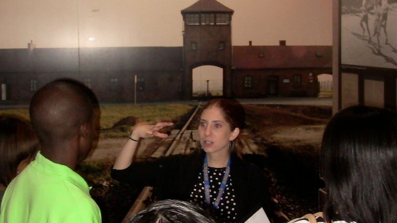 Volunteer Beth Brown, standing in front of a photo of the Auschwitz-Birkenau concentration camp, explains the Holocaust to students from Columbus High School recently at the William Breman Jewish Heritage and Holocaust Museum in the downtown area.