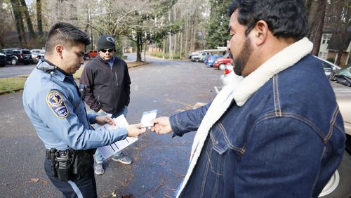 Sr. Officer Daniel Arrata talks in Spanish with Gwinnett residents Gilberto Perez, center, and Ricardo Salmeron; Officer Arrata helped investigate a VIN number from a vehicle Perez tried to sell to Salmeron.
 Miguel Martinez / miguel.martinezjimenez@ajc.com