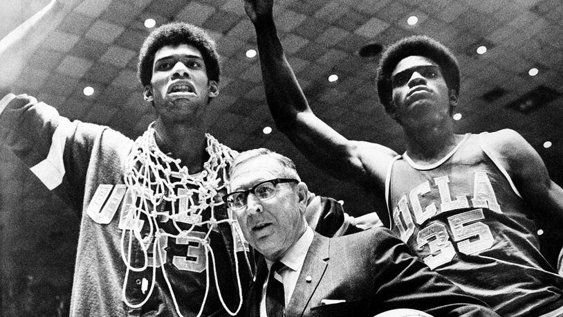 In this March 24, 1969, file photo, UCLA coach John Wooden is flanked by Sidney Wicks, right, and Lew Alcindor, draped with the nets, after the Bruins beat Purdue 92-72 to win the NCAA title for the third consecutive year.