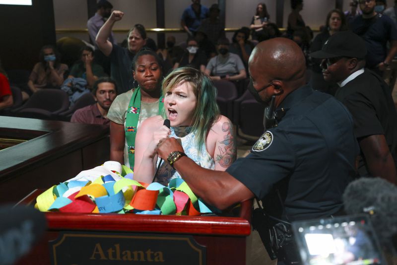 An Atlanta Police officer, right, attempts to remove the microphone from a protester as she speaks during the extended public comment portion ahead of the final vote to approve legislation to fund the training center, on Monday, June 5, 2023, in Atlanta. (Jason Getz / Jason.Getz@ajc.com)