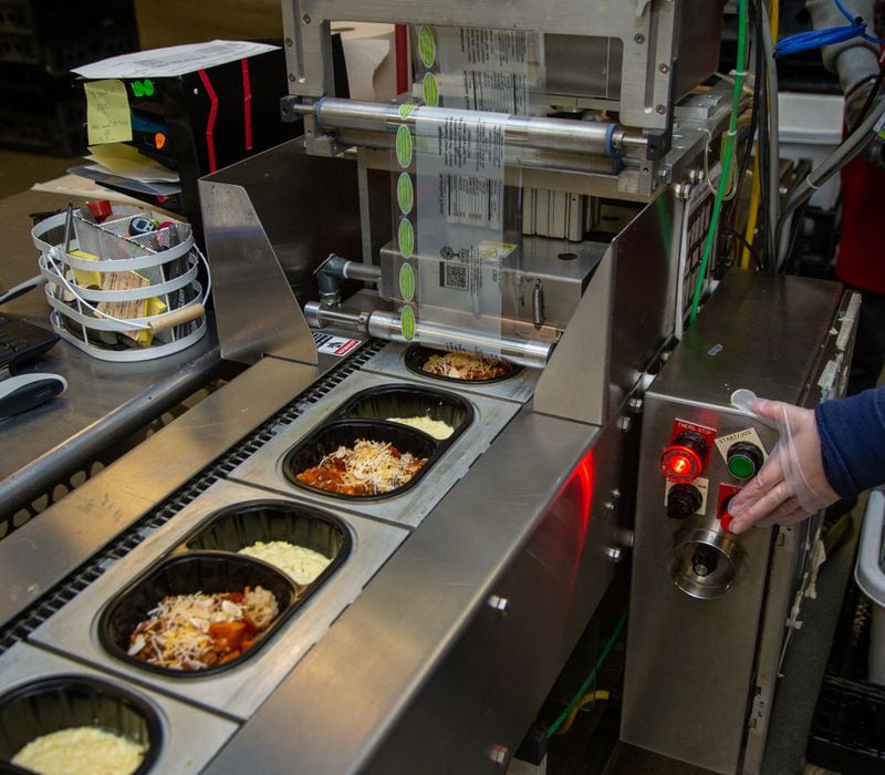 A worker controls the machine that seals meals at Open Hand Atlanta. PHIL SKINNER FOR THE ATLANTA JOURNAL-CONSTITUTION.