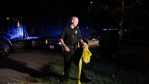 A DeKalb County police officer replaces police line tape at the entrance of a condominium community near Decatur on Friday morning after a man was shot during a robbery.