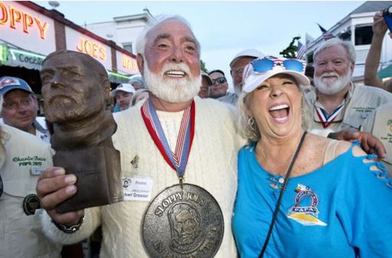 In this Saturday, July 21, 2018, photo provided by the Florida Keys News Bureau, Michael Groover, left, husband of celebrity chef Paula Deen, right, walks off the stage after competing in the semi-final round of the Hemingway Look-Alike Contest at Sloppy Joe's Bar in Key West, Fla. On his eighth attempt, Groover won the competition, the highlight event of the island city's annual Hemingway Days festival.