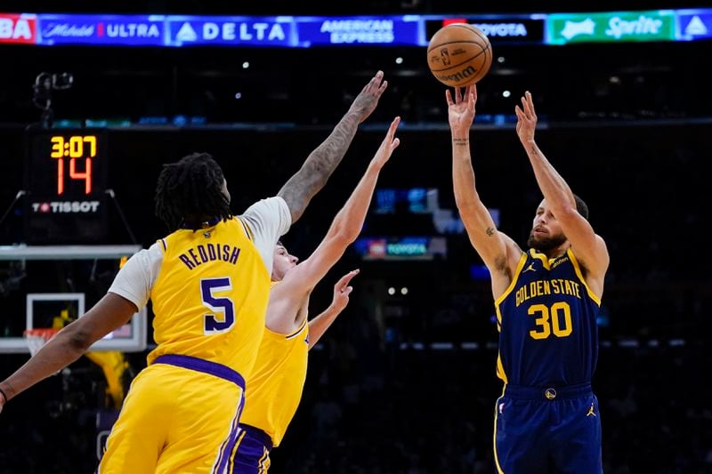 Golden State Warriors guard Stephen Curry, right, shoots againstLos Angeles Lakers forward Cam Reddish, left, and guard Austin Reaves during the first half of an NBA basketball game Tuesday, April 9, 2024, in Los Angeles. (AP Photo/Ryan Sun)