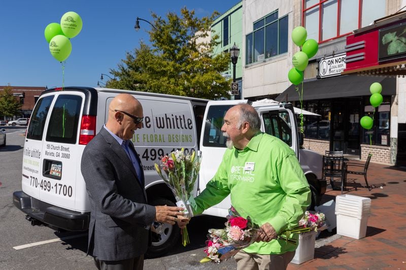 Florist K. Mike Whittle hands flowers to Cobb County Superior Court Judge Vic Reynolds in Marietta Square on Wednesday, October 18, 2023. The event was part of the Society of American Florists' “Petal it Forward” goodwill initiative. (Arvin Temkar / arvin.temkar@ajc.com)
