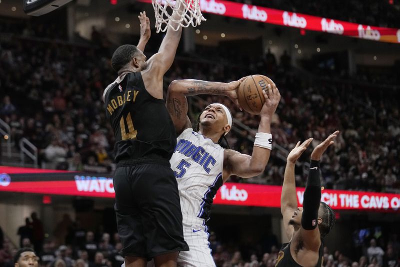 Orlando Magic forward Paolo Banchero (5) is defended by Cleveland Cavaliers forward Evan Mobley and forward Isaac Okoro, right, in the second half of Game 7 of an NBA basketball first-round playoff series, Sunday, May 5, 2024, in Cleveland. (AP Photo/Sue Ogrocki)