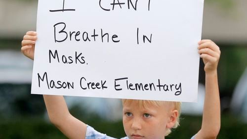 Reily McCormick, 8, holds out a sign outside the Douglas County Board of Education to protest a mask mandate as a school bus passes by on Wednesday, August 4, 2021. Douglas County Schools approved the measure that requires mask use in schools and on buses Monday during a board of education meeting. Parents expressed their frustration with the rule, saying masks have been damaging for their children because they make it difficult to breathe and to socialize with other kids. “They distract me from learning because I can’t breathe,” McCormick said. His parents allowed him to skip school in the morning to participate in the protest but said they would be dropping him off for the first day of school at the end.  “He wanted to make his voice heard,” his father Thomas McCormick said. (Christine Tannous / christine.tannous@ajc.com)