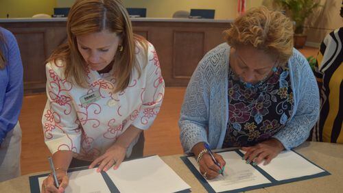 Board of Education chair Holly Cobb and Board of Commissioners chair Carlotta Harrell sign the agreement.