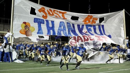 McEachern players run out of a banner that reads, "Just be thankful you made it this far," before their game against North Gwinnett in the Class 7A quarterfinals at McEachern High School Friday, Nov. 29, 2019, in Powder Springs.