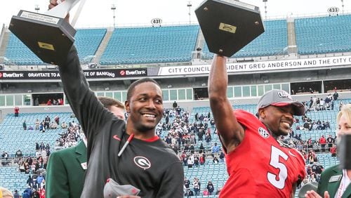 Georgia interim head coach Bryan McClendon, left, with game trophy and wide receiver Terry Godwin (5) with the MVP trophy, celebrated after defeating Penn State 24-17 in the TaxSlayer Bowl on Saturday, Jan. 2, 2016, in Jacksonville, Fla. Georgia won 24-17. (Gary Lloyd McCullough/The Florida Times-Union via AP)