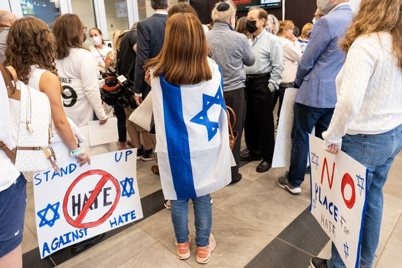 Claudia Rolam, wrapped in the Israeli flag,  protests outside of the Cobb County School Board meeting Thursday evening, Sept. 23, 2021, after antisemitic vandalism was discovered at two Cobb County High Schools. Rolam is a member of Temple Emanuel in Atlanta. Ben Gray for the Atlanta Journal-Constitution