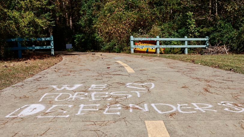Text that reads We Love Forest Defenders is written on a sidewalk near forested area that is the proposed site of Cop City as seen on Friday, October 21, 2022. (Natrice Miller/natrice.miller@ajc.com)  