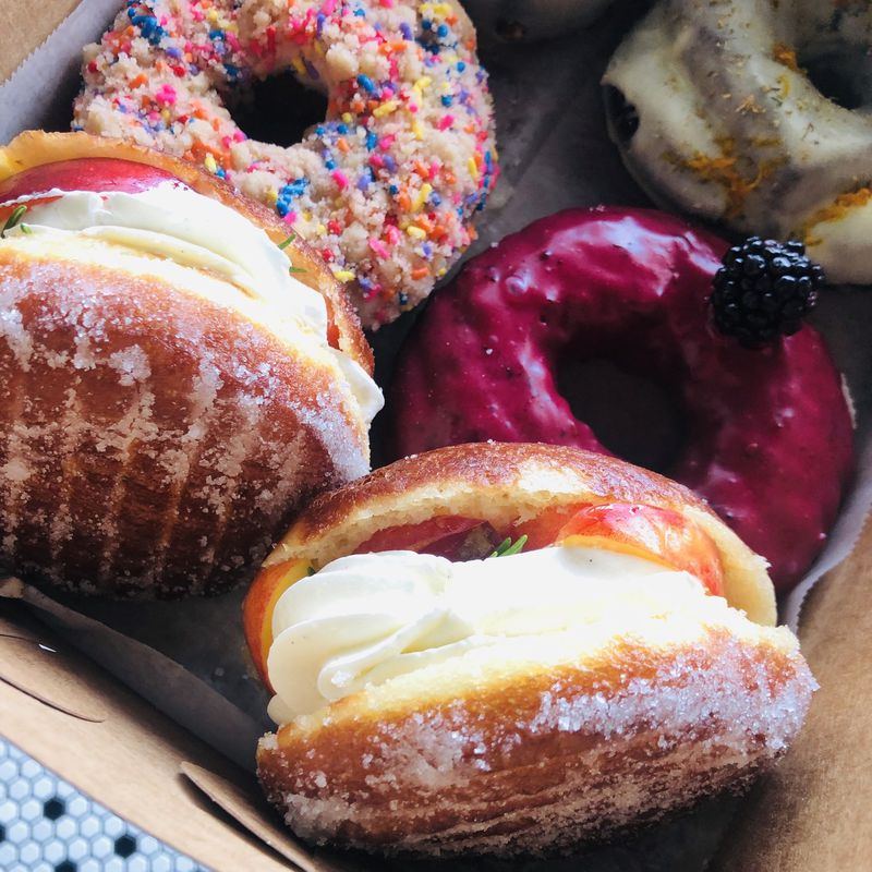 Among the treats at Doughnut Dollies are fresh nectarine and raspberry shortcake doughnuts in the foreground (a seasonal specialty) and glazed Bismarcks filled with buttercream and slices of nectarine. CONTRIBUTED BY DOUGHNUT DOLLIES
