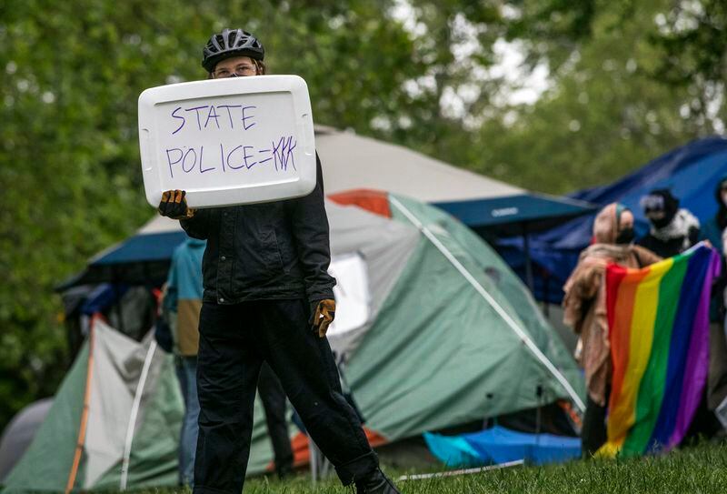 A pro-Palestinian supporter holds a sign reading "State Police=KKK" on the grounds of the University of Virginia, in Charlottesville, Va., where they set up tents, Saturday, May 4, 2024. (Cal Cary/The Daily Progress via AP)