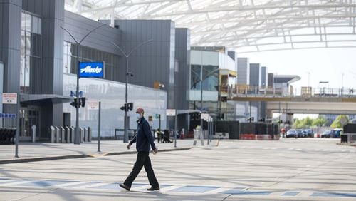 A man wearing a mask walks along a crosswalk in a nearly empty airport arrivals entrance at Hartsfield-Jackson International Airport in Atlanta, Tuesday, April 14, 2020. (ALYSSA POINTER / ALYSSA.POINTER@AJC.COM)
