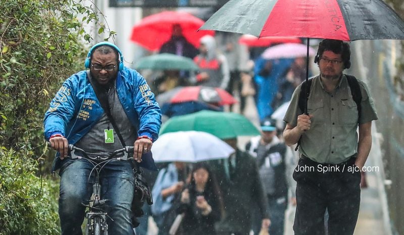 Joel Meyer (left) did not have an umbrella Thursday morning for his commute from the Buckhead MARTA station to the Atlanta Tech Village. JOHN SPINK / JSPINK@AJC.COM