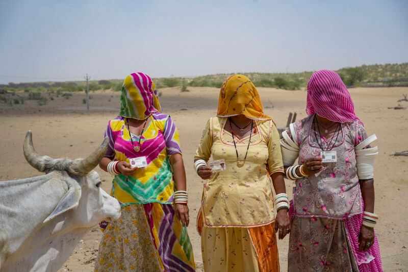 Women pose with their identity cards as they walk to cast their vote during the second phase of polling in the six-week long national election in the desert village Jaiisindhar, Barmer district, western Rajasthan state, India, Friday, April 26, 2024. (AP Photo/Deepak Sharma)