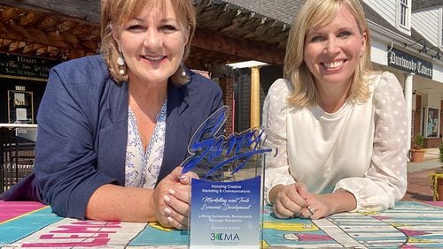 Dunwoody Communications Manager Kathy Florence and Dunwoody Communications Director Jennifer Boettcher pose with the Savvy Award at a painted picnic table in the Dunwoody Village. CONTRIBUTED