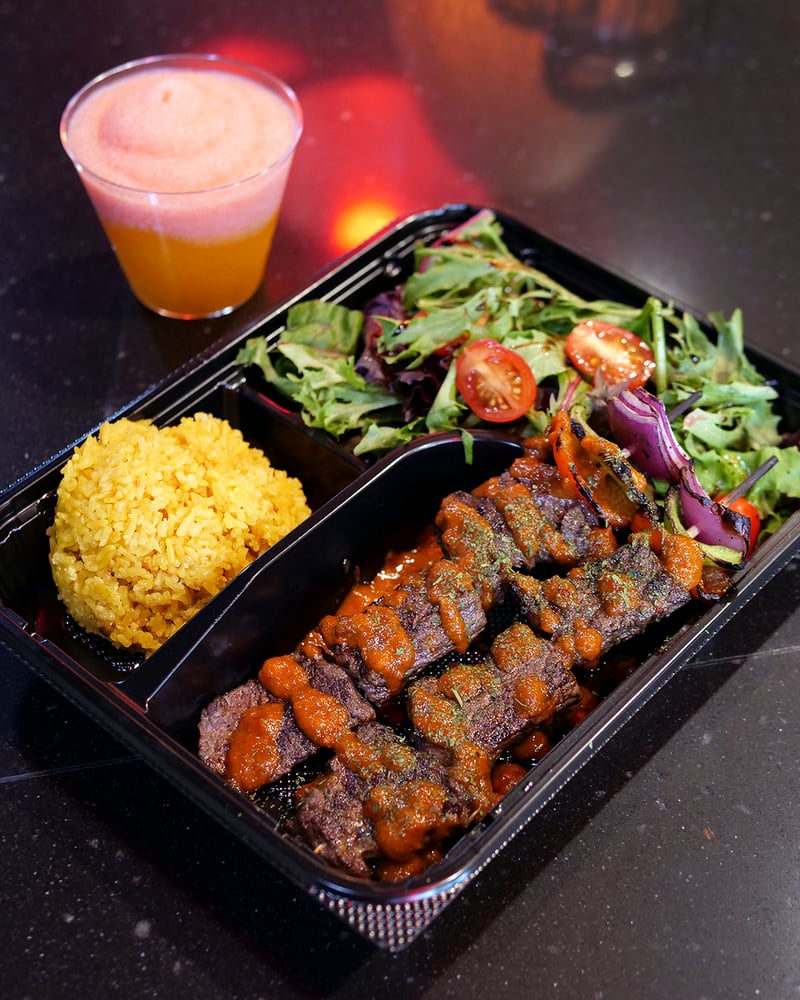 Osha Farm Grill offers a concise menu of skewered proteins. Pictured are rib-eye skewers drizzled with a smoked red pepper sauce, yellow garlic rice, and a mixed greens salad. (Courtesy of Julius Mayo)
