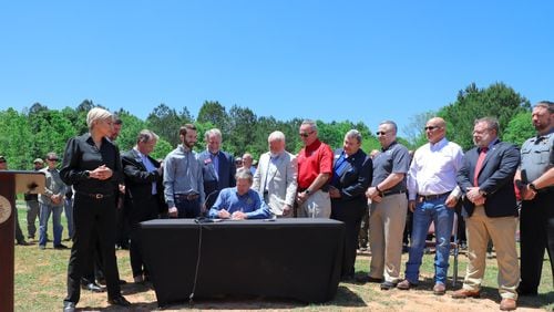Gov. Brian Kemp, surrounded by state legislators and law enforcement officers at the Barrow County Sheriff's Office gun range, signs a bill into law Friday banning deep cuts into police budgets. Credit: Georgia governor's office