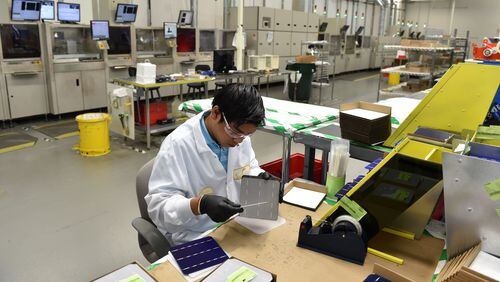 Norcross-based Suniva said it is cutting jobs after overseas competition and other challenges have hurt sales. Here, Nishan Kharga at Suniva’s Norcross factory performs a quality control inspection of solar cells before they are shipped out for assembly in solar panels. BRANT SANDERLIN /BSANDERLIN@AJC.COM