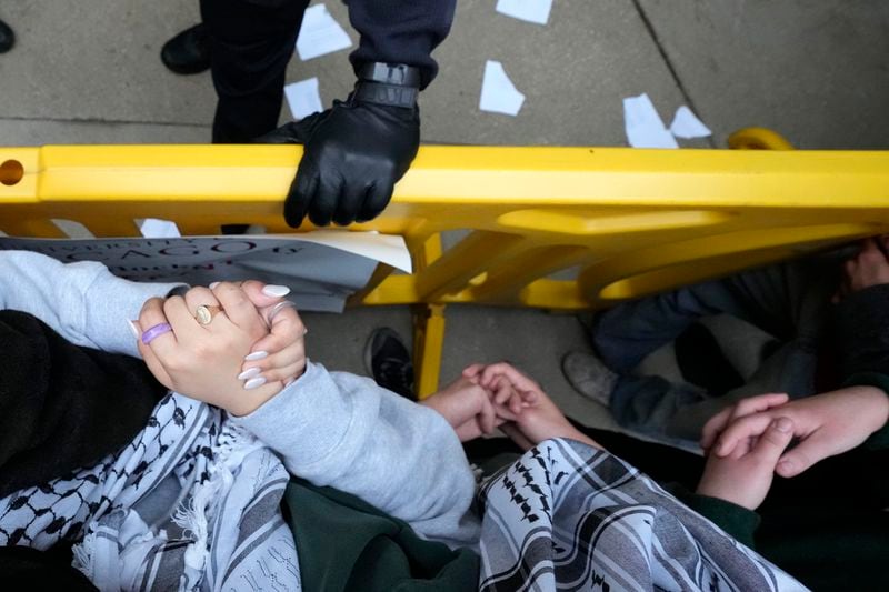 Pro-Palestinian protesters lock arms and clasp their hands as a University of Chicago police officer holds onto a barricade while officers kept protesters from the university's quad while the student encampment is dismantled Tuesday, May 7, 2024, in Chicago. (AP Photo/Charles Rex Arbogast)