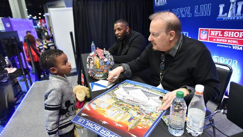 The NFL's official Super Bowl artist Charles Fazzino signs an autograph for fan Kingston Morton at the NFL shop during Super Bowl Experience inside the Georgia World Congress Center on Wednesday, January 30, 2019.