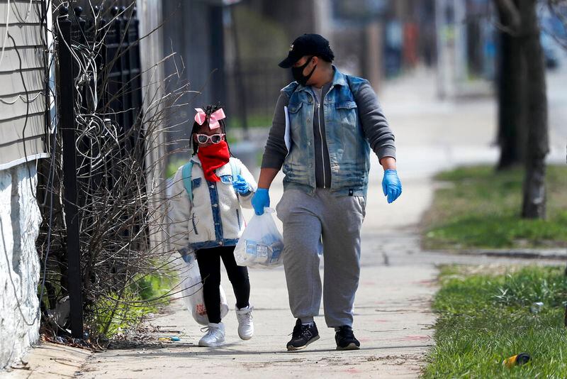 In this April 7, 2020, photo, Erica Harris, right, and her daughter Jordan, wear their protective masks as they walk back home after getting a lunch and homework from the childâs school on Chicagoâs Southside in Chicago. As the coronavirus tightened its grip across the country, it is cutting a particularly devastating swath through an already vulnerable population, black Americans. (AP Photo/Charles Rex Arbogast)